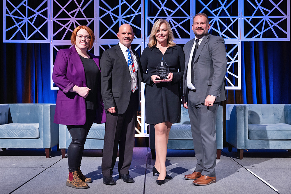 four people standing on a stage, one with an award in hands