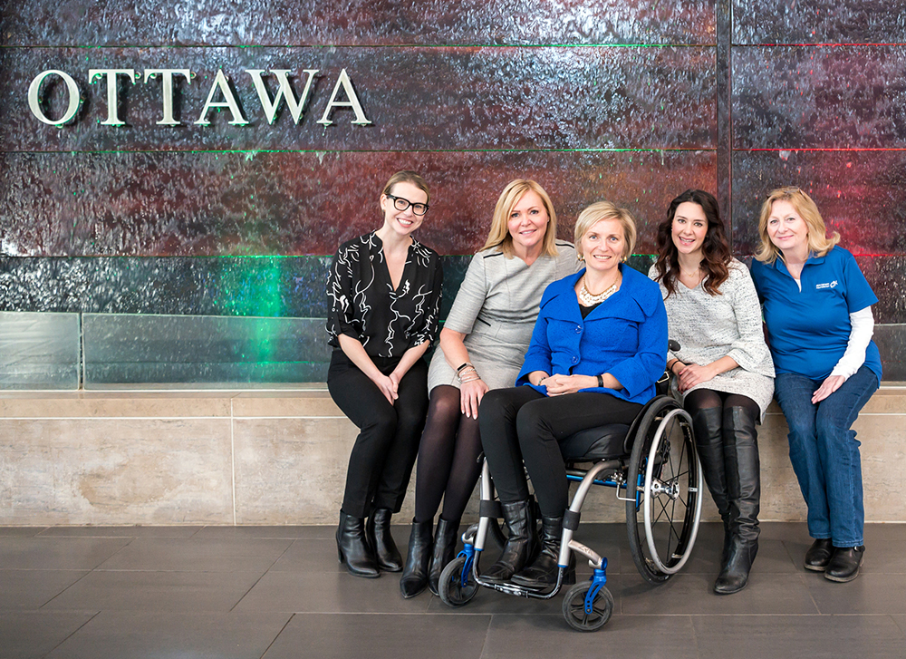 Sarah McCarthy, Krista Kealey, Julie Sawchuk, Samantha Proulx, Mardelle Woods siting in front of Ottawa locks in the Arrival area at the Ottawa Airport